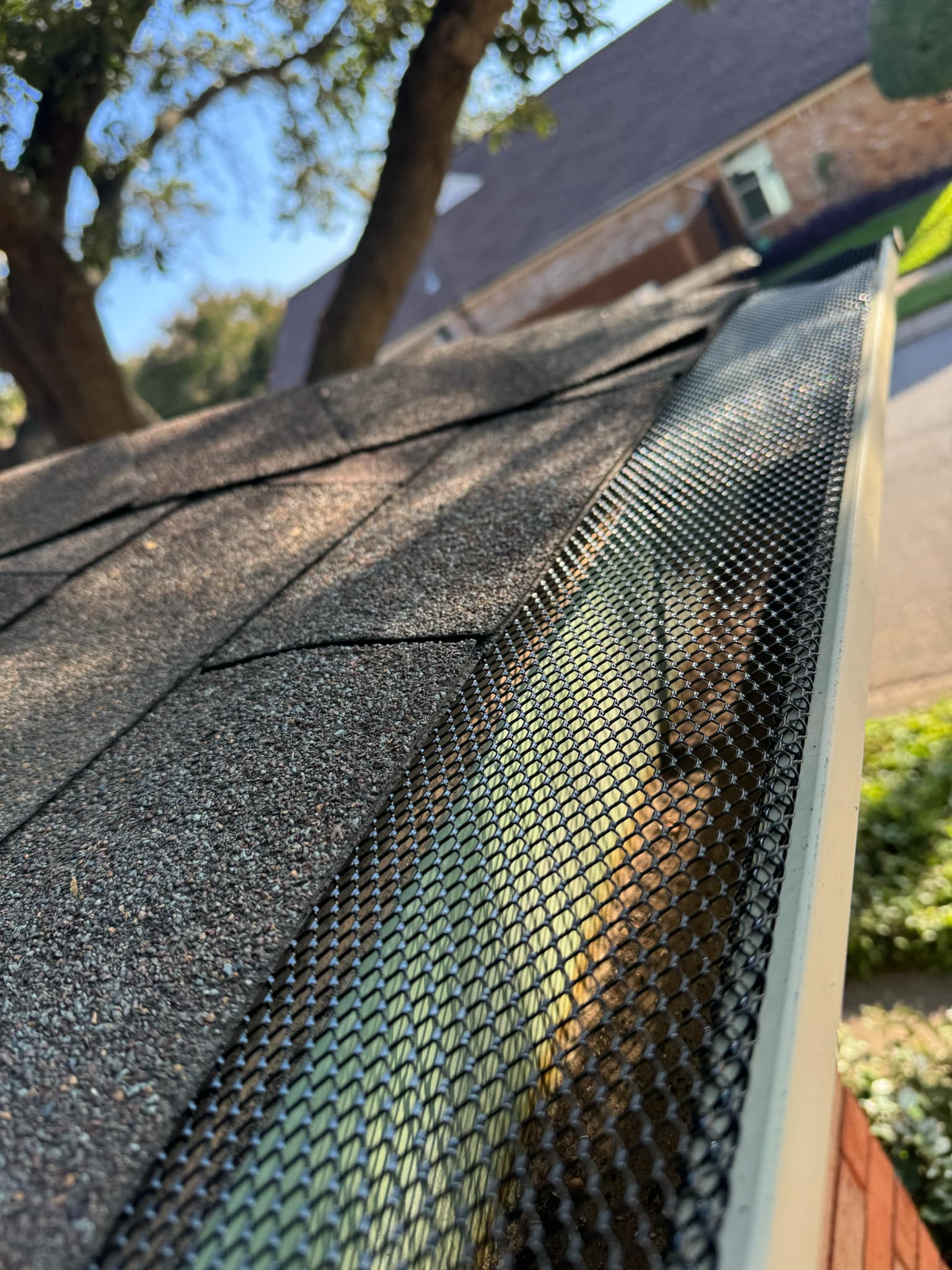 Close-up of black diamond-mesh leaf guard installed over a DFW home's gutter, roof shingles visible