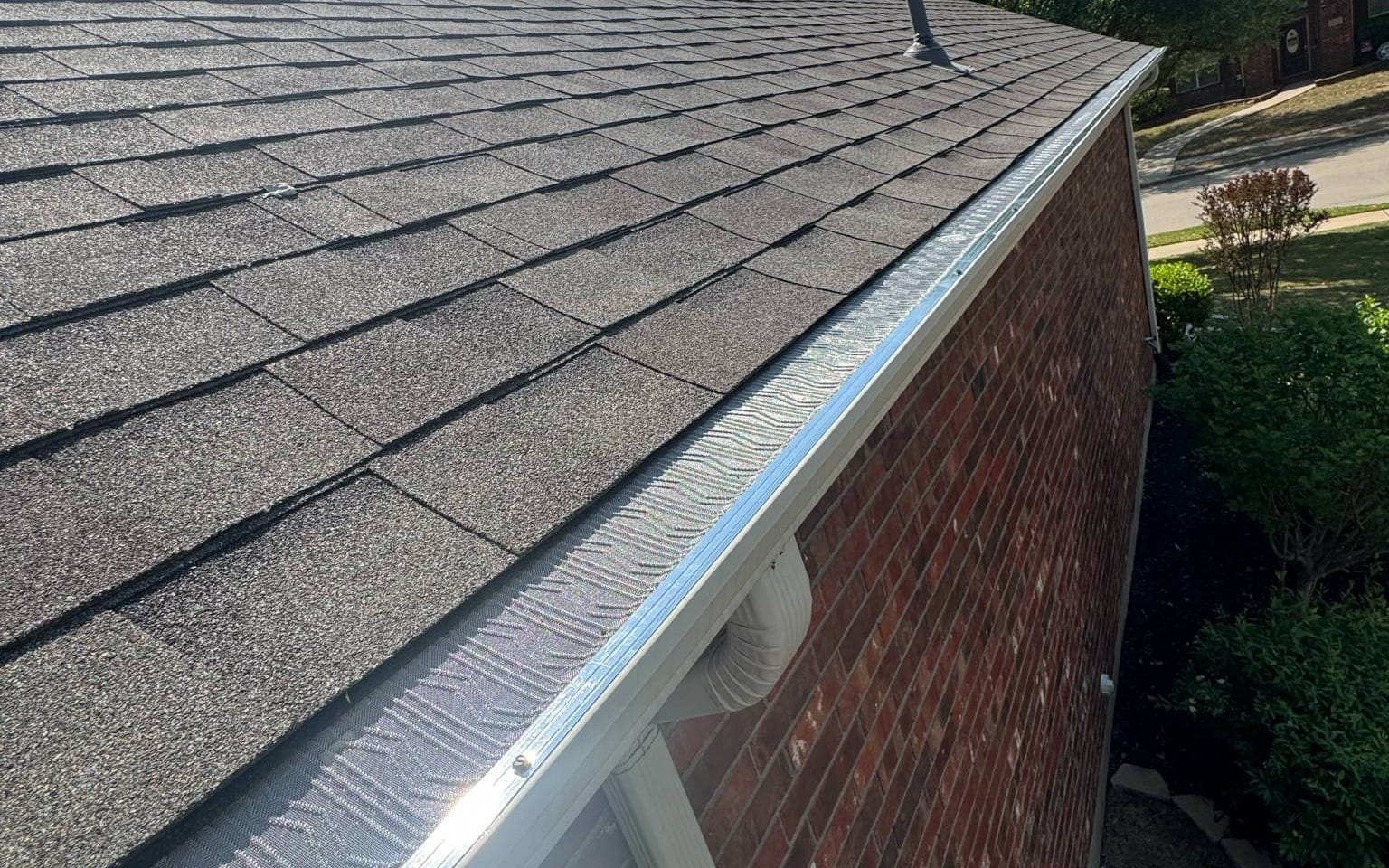 Leaf guard mesh installed along the roofline of a different DFW brick home, gutter and downspout visible